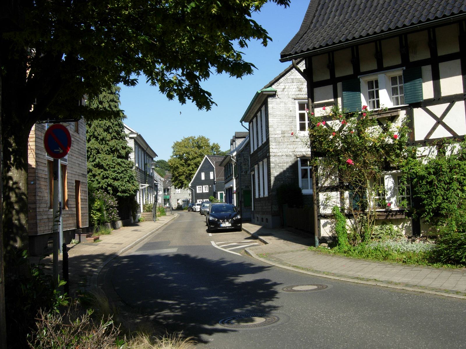 In der Mittelstraße stehen verschiedene Fachwerkhäuser und verschieferte Häuser. Autos parken am Straßenrand.